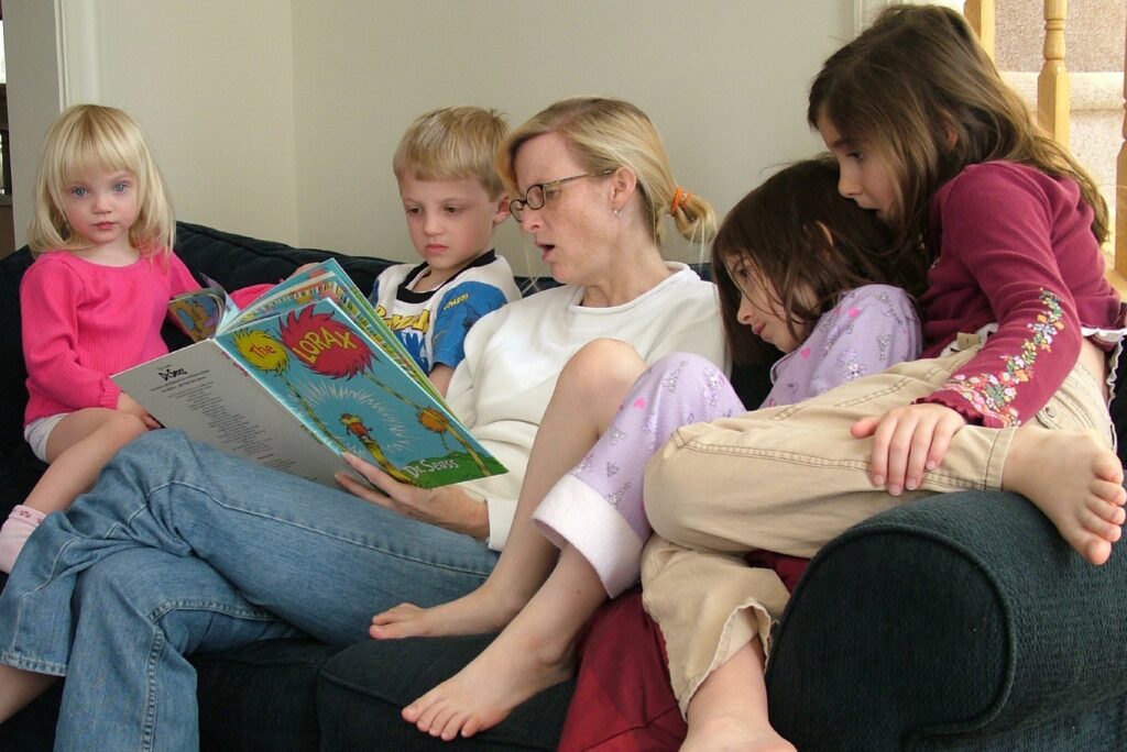 woman reading a book to four children on a couch