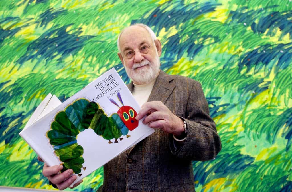 author eric carle holding a copy of his book, the very hungry caterpillar