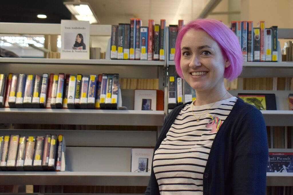 woman smiling for a photo in front of bookshelves