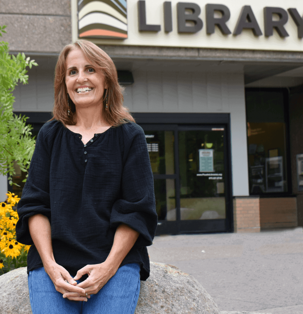 woman smiling and sitting on a rock outside a library