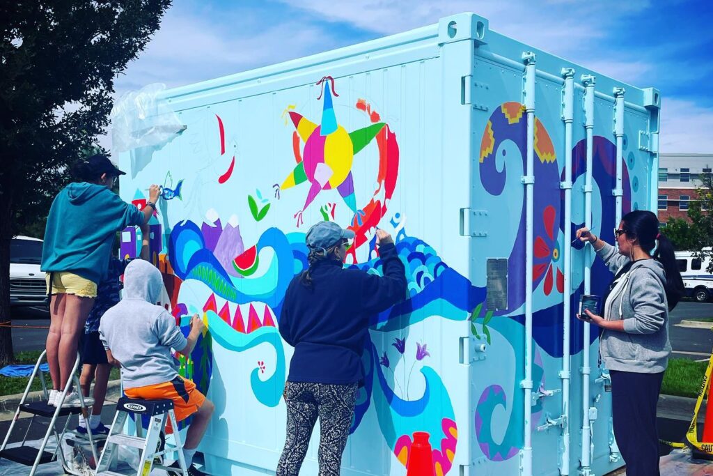 group of people painting a mural on a container