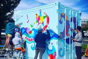 group of people painting a mural on a container