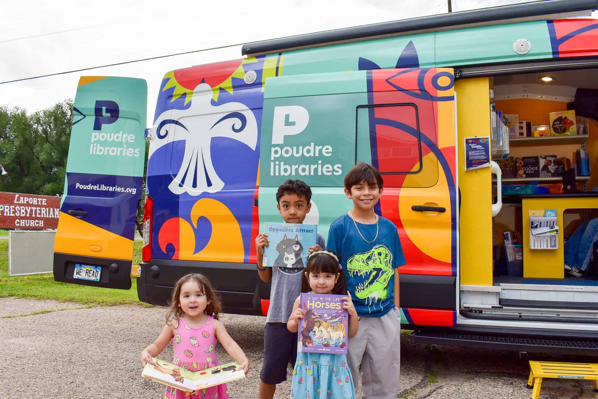 Two young girls and two young boys smiling with picture books in front of a colorful van