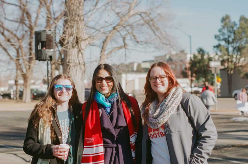 Three women smiling with jackets and scarves on outside