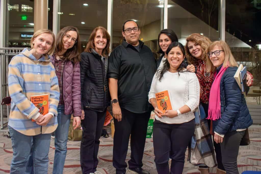 A group of eight women smiling, some holding books smiling next to a male author