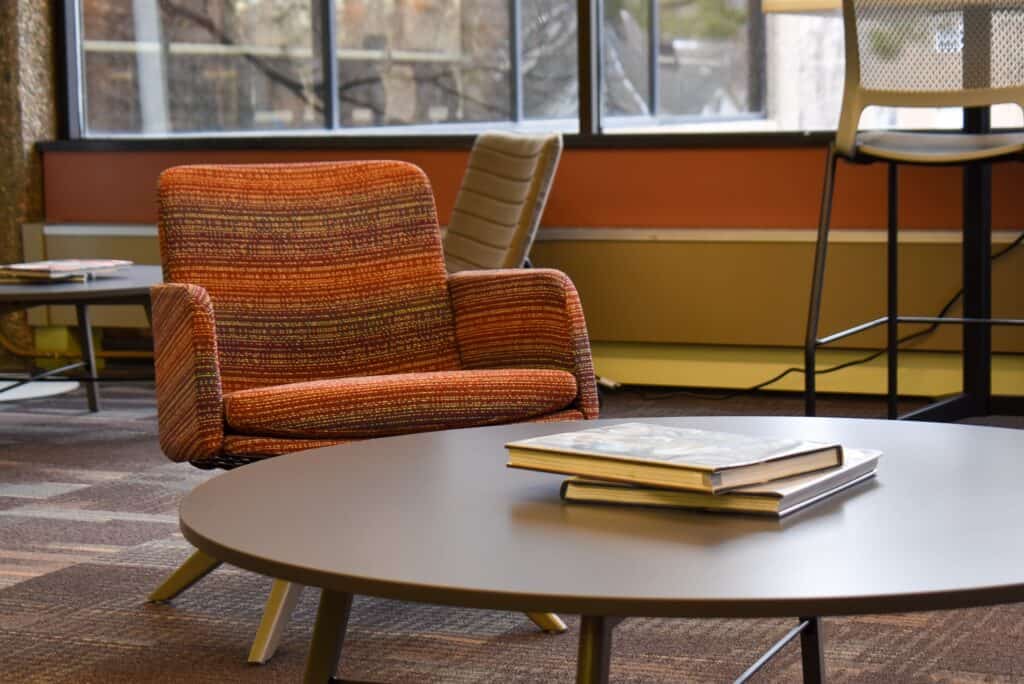 Upholstered red and cream chair in front of a low-to-the-ground grey table with two hardcover books on it.