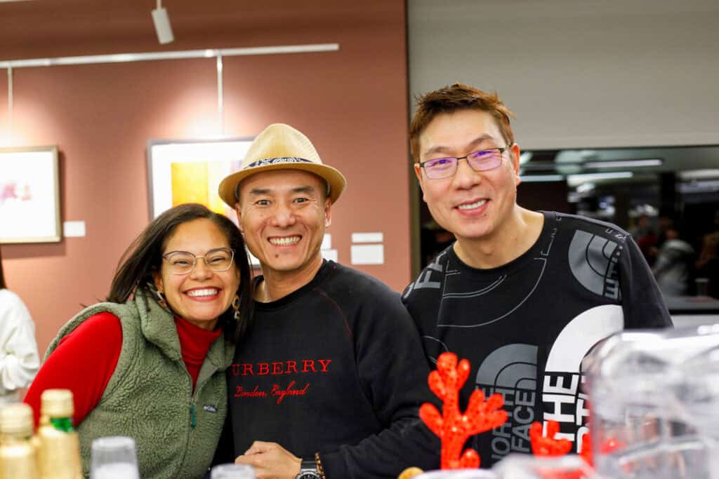 Two men smiling next to a smiling woman posing for a photograph