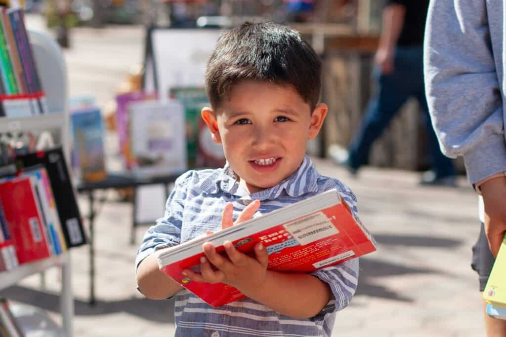 Young boy holding a red book outdoors