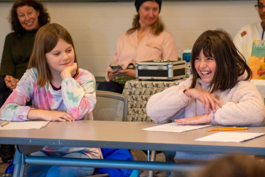 Two young girls smiling while seated at a table