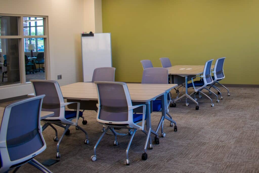 Large meeting room with grey tables, chairs, and a whiteboard