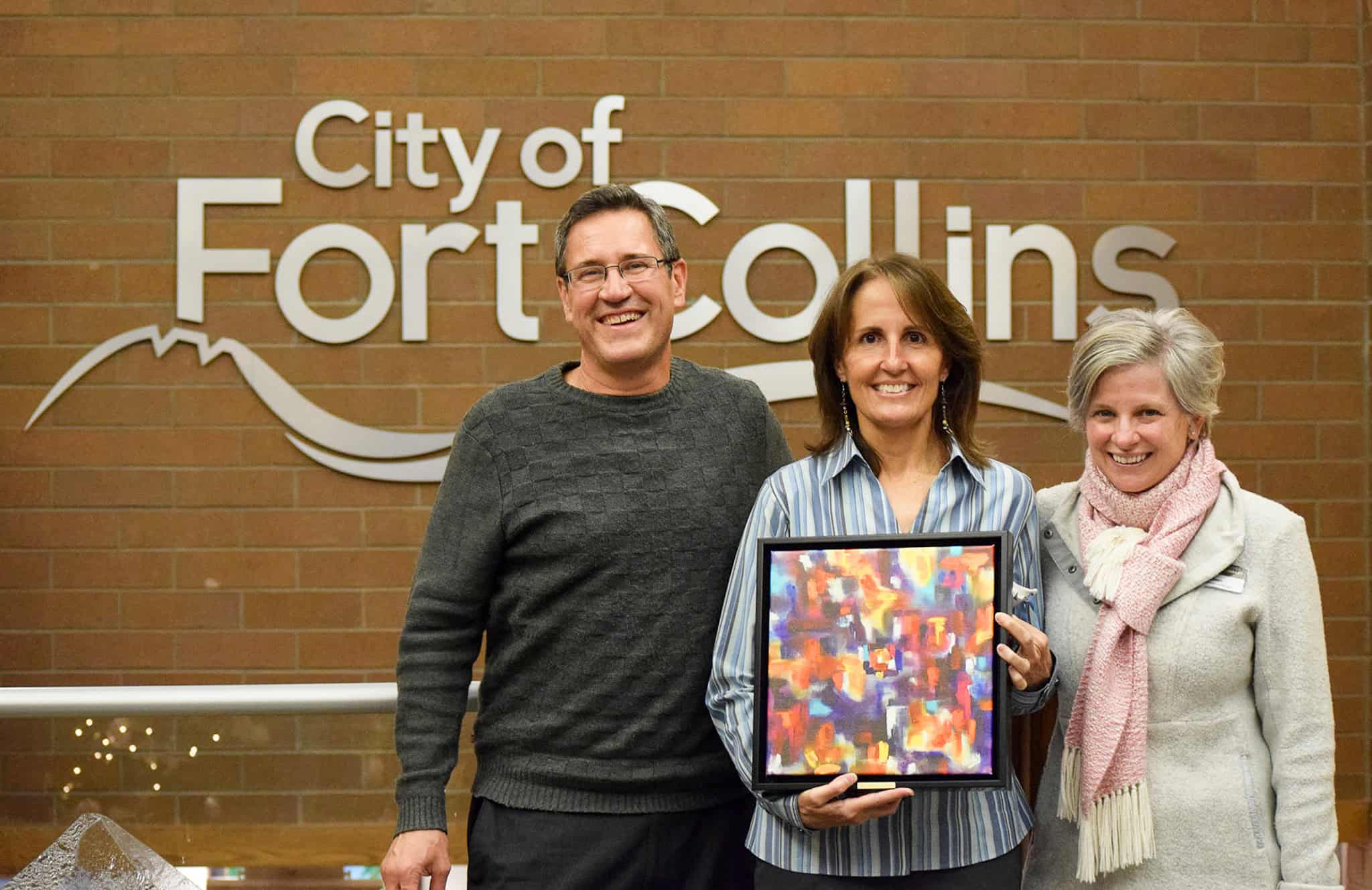 Woman holding a colorful painting between another man and woman.