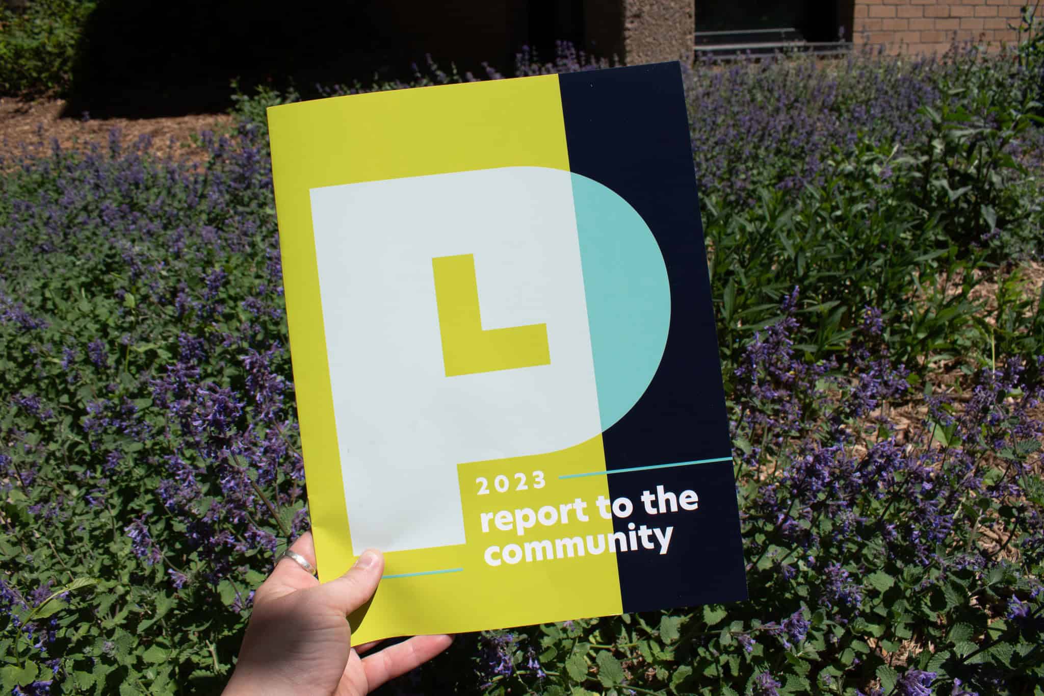 Hand holding a library report to the community booklet in front of flowers