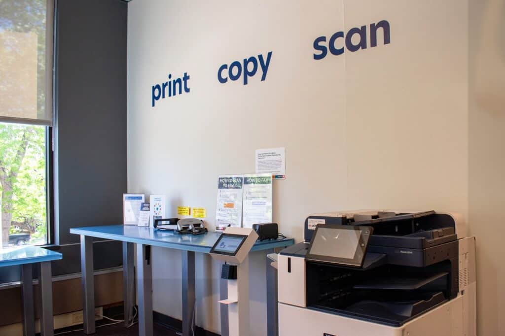 Wall with the words print, copy, scan on it directly above a printer and table