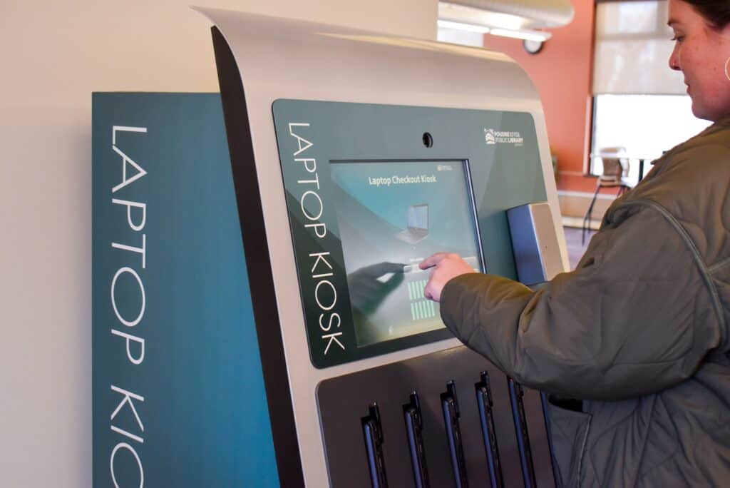 Woman clicking the screen on a teal and silver laptop checkout machine