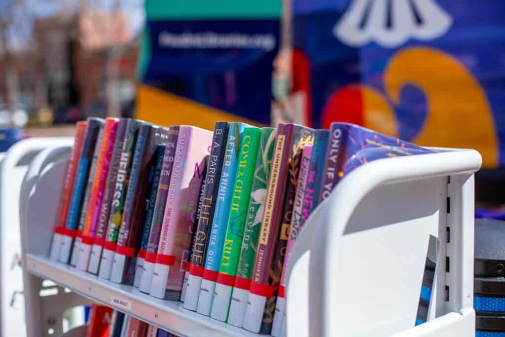 Libros de tapa dura de colores en un carro blanco de libros de biblioteca.