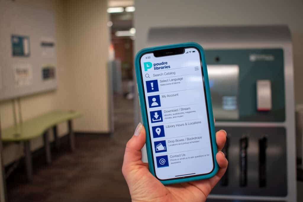 a hand holding up an iphone displaying poudre libraries app