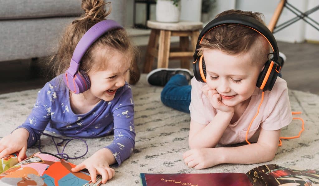 Two young children wearing headphones while reading books