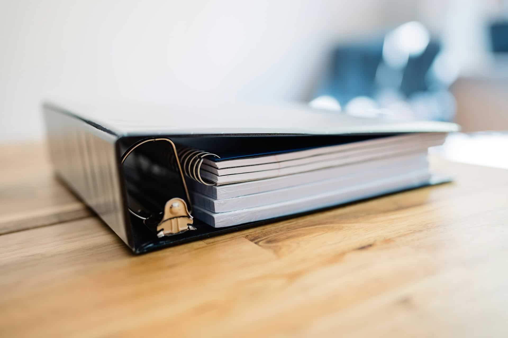 navy colored binder holding stacks of paper sitting on a wooden table