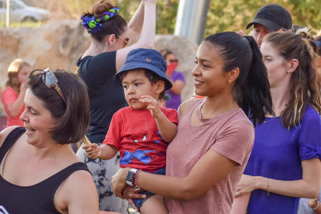 Mother holding her young son with various adults in the background