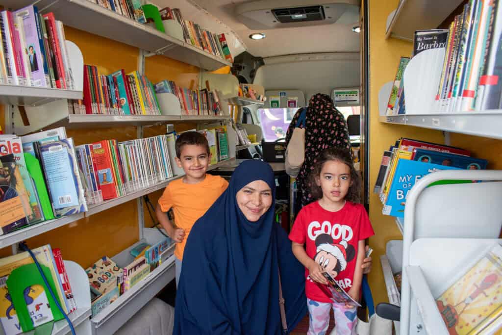 Una madre y sus dos hijos sonríen para una foto dentro del bibliobús de una biblioteca