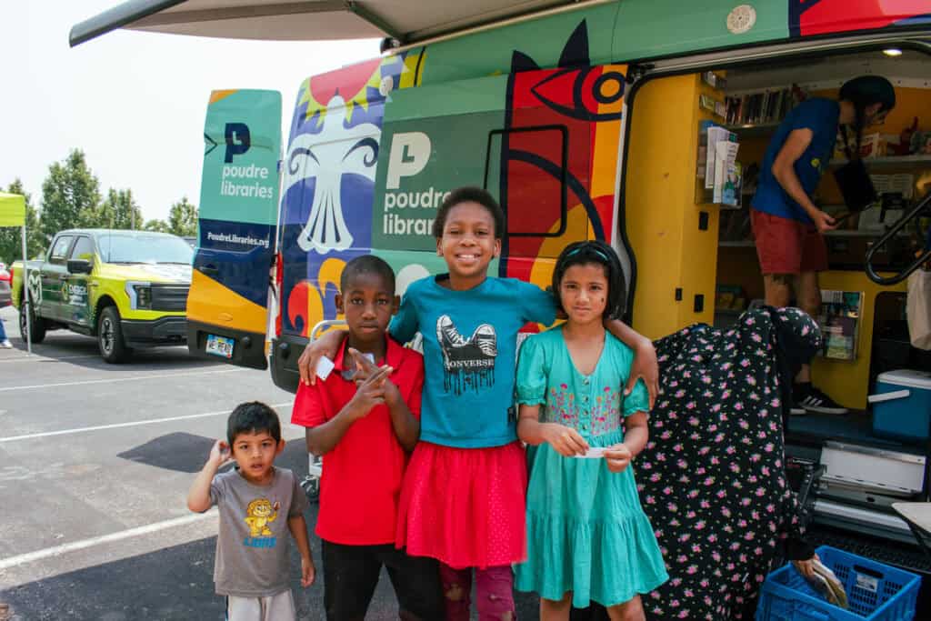 Grupo de cuatro niños sonriendo para una foto delante de un colorido bibliobús.