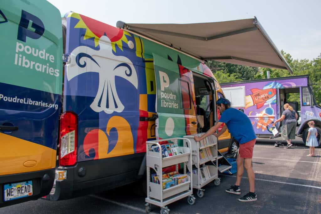 Male library employee setting up book carts in front of "Evie," a colorful library bookmobile