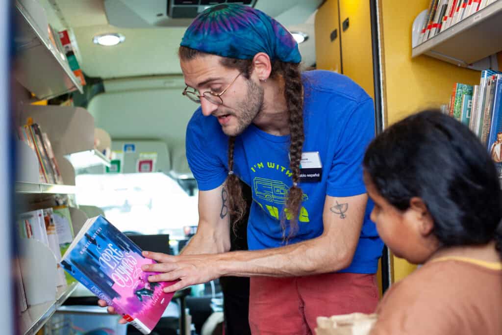 Male library employee shows a young girl a book inside a library bookmobile