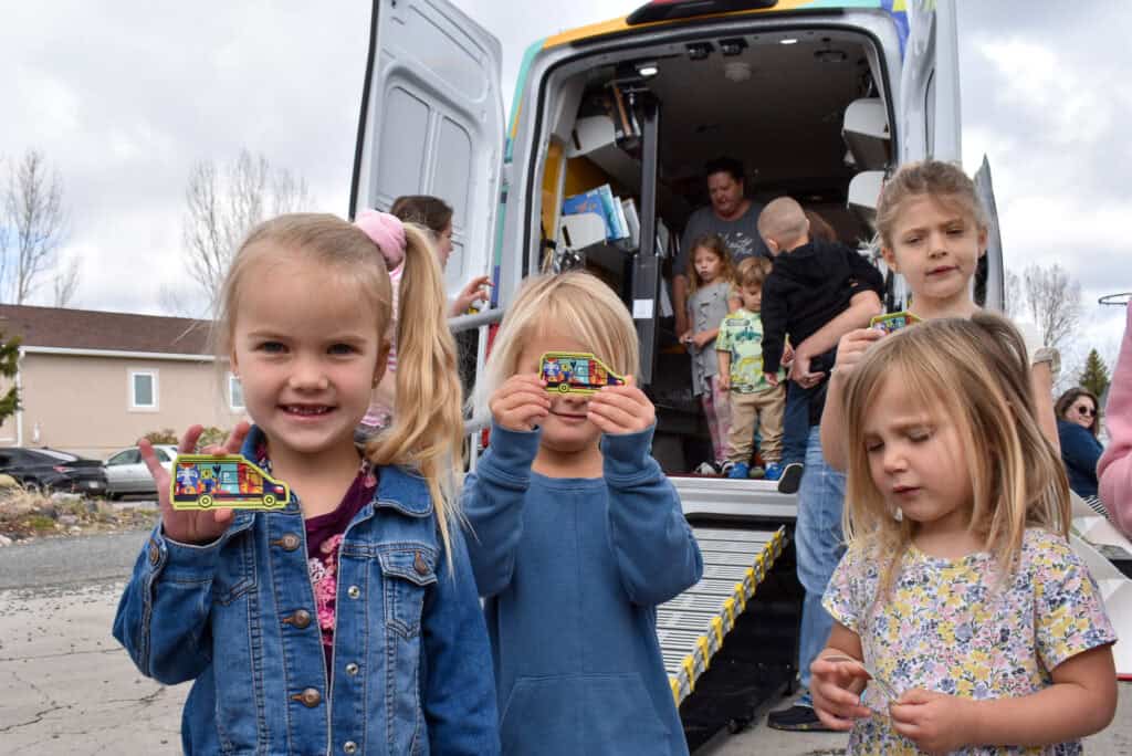 Young girls holding library bookmobile stickers in front of "Evie," the library bookmobile