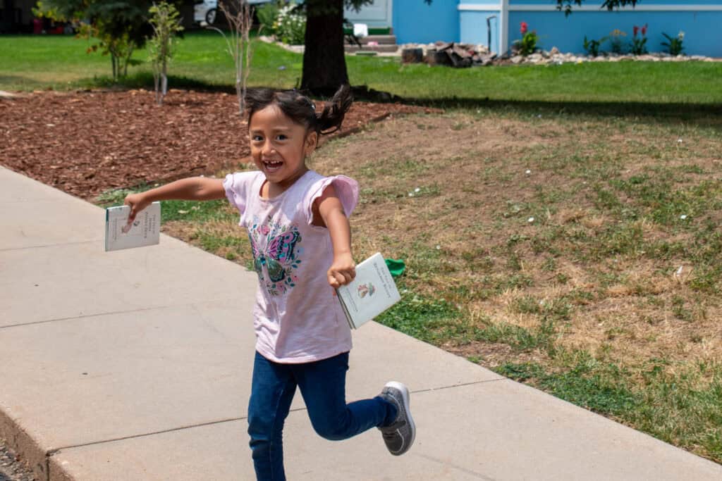 Little girl running outdoors with two books in her hands