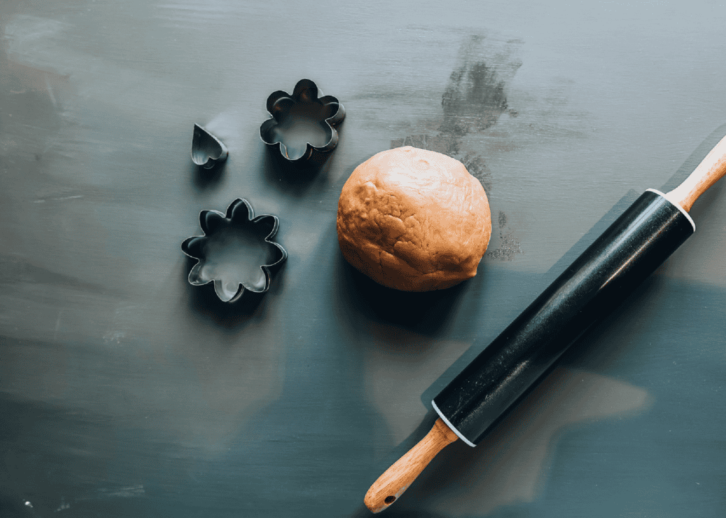 Rodillo negro junto a una bola de masa para galletas y cortapastas