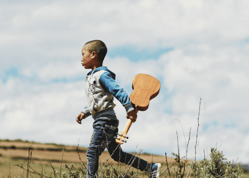 Niño con un ukelele en la mano mientras corre al aire libre