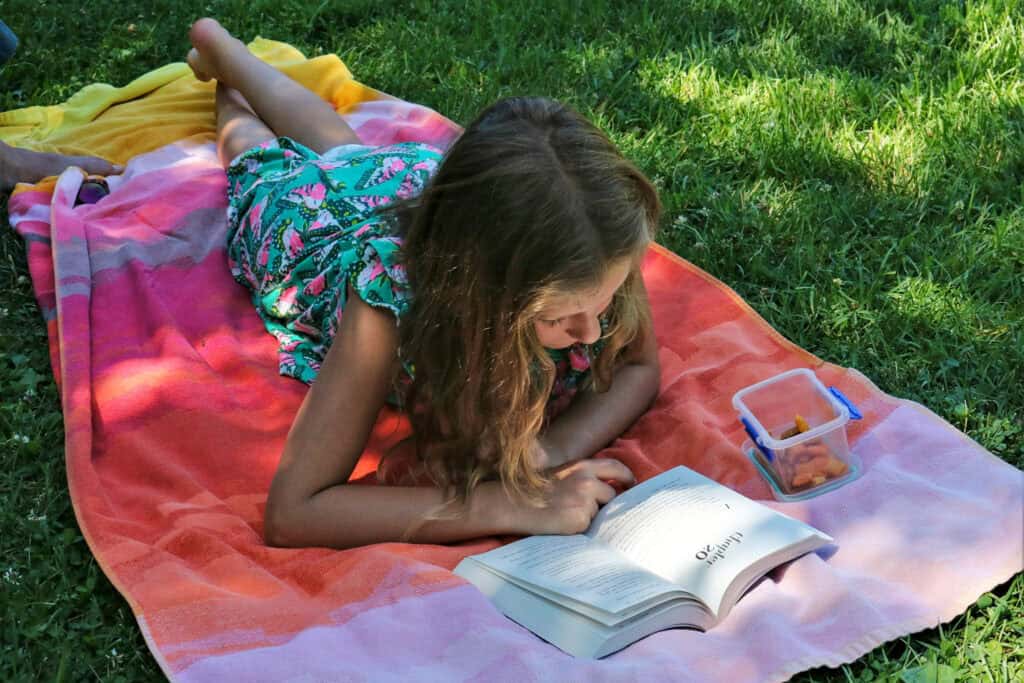 Young girl reading on a colorful towel on the grass