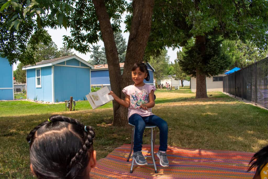 Young girl reading to others outdoors