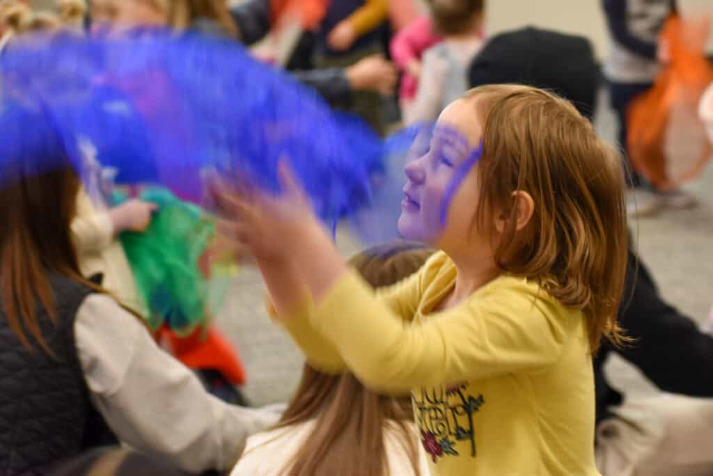 Niña lanzando un pañuelo azul al aire en una hora de cuentos en la biblioteca