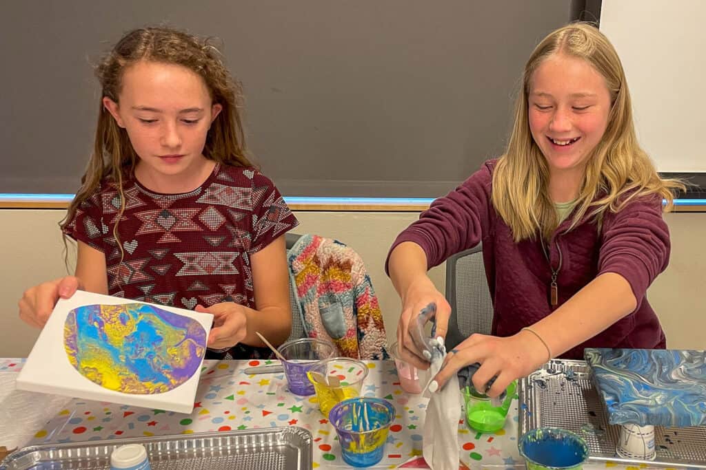 Two teenage girls pouring colorful paint on canvases