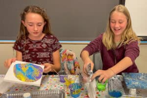 Two teenage girls pouring colorful paint on canvases