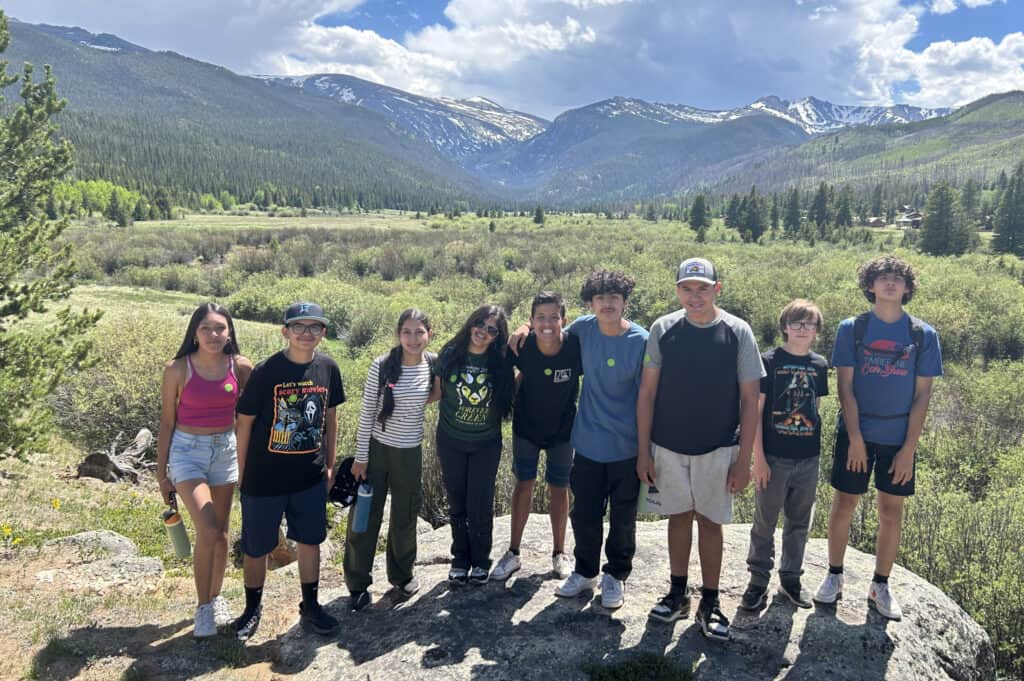 A group of teens smiling for a photo in a field with mountains in the background