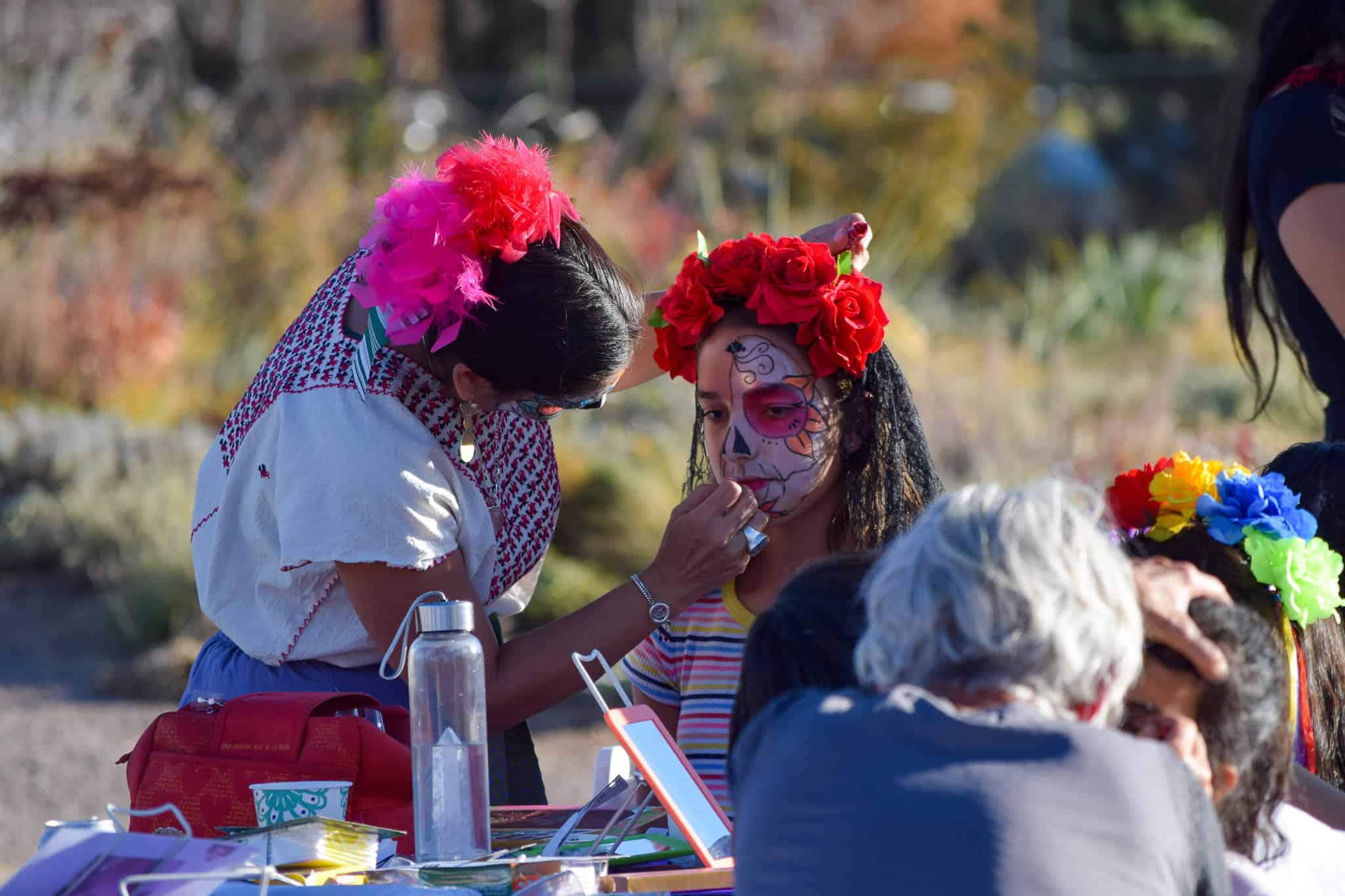 Woman painting a little girl's face for dia de muertos.