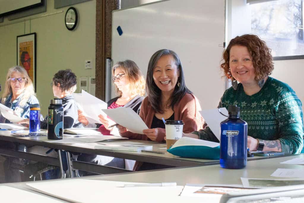 Two women smiling for a photo and holding pieces of paper in at a writing workshop