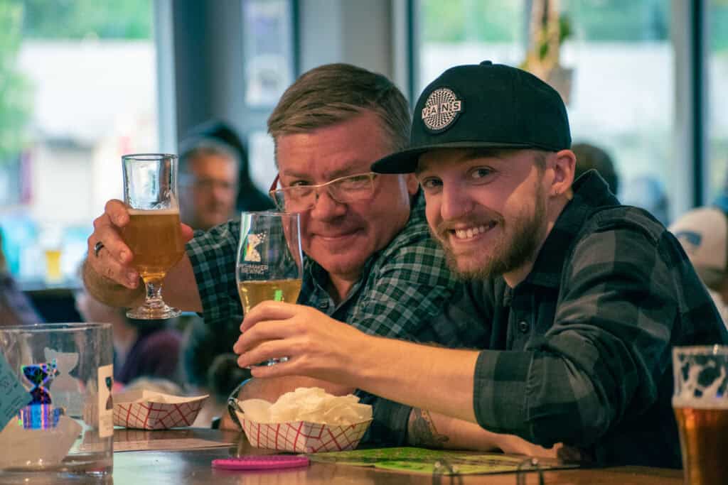 Two men smiling for a photo and holding up their beverages