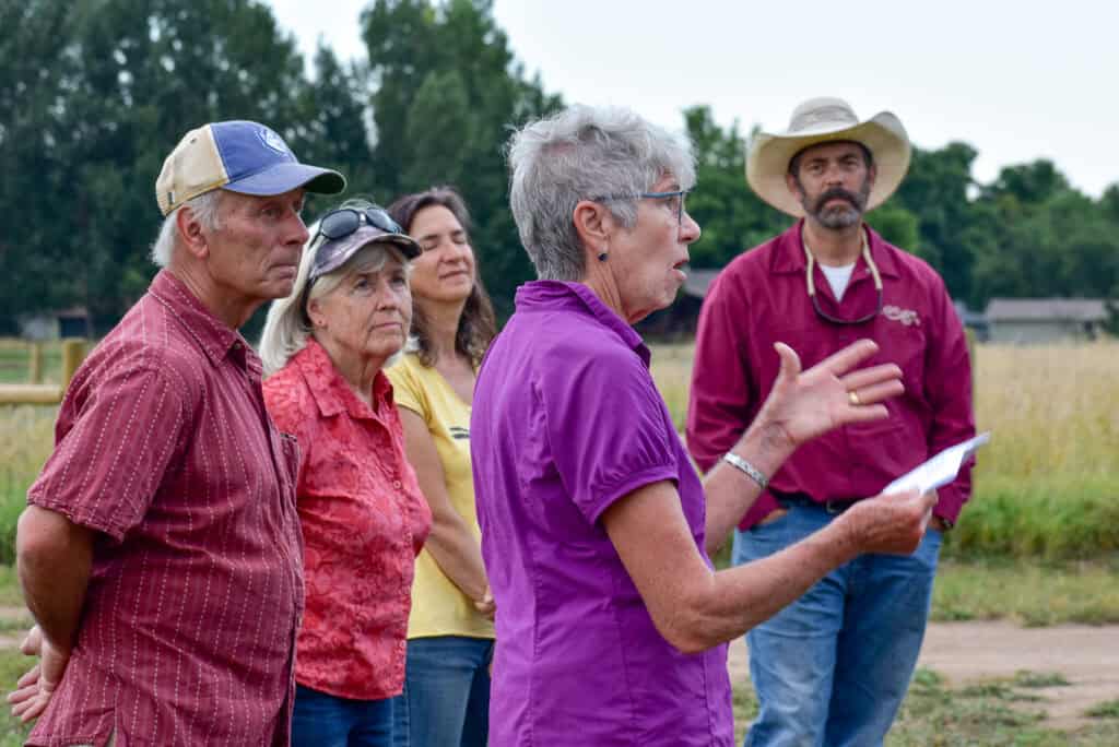 Older woman with a piece of paper in her hand talking to a group of adults outside