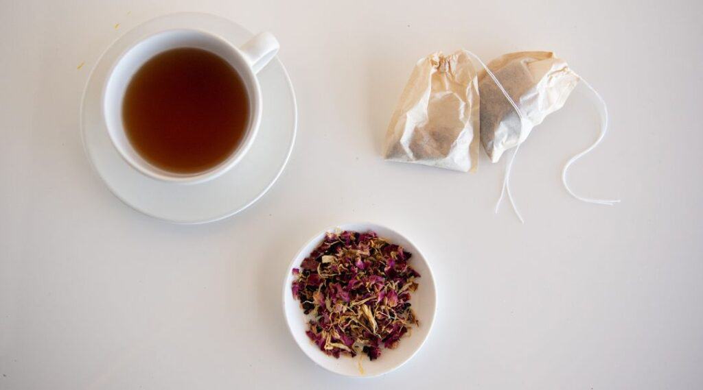 Una taza de té junto a bolsitas y un cuenco de hojas de té