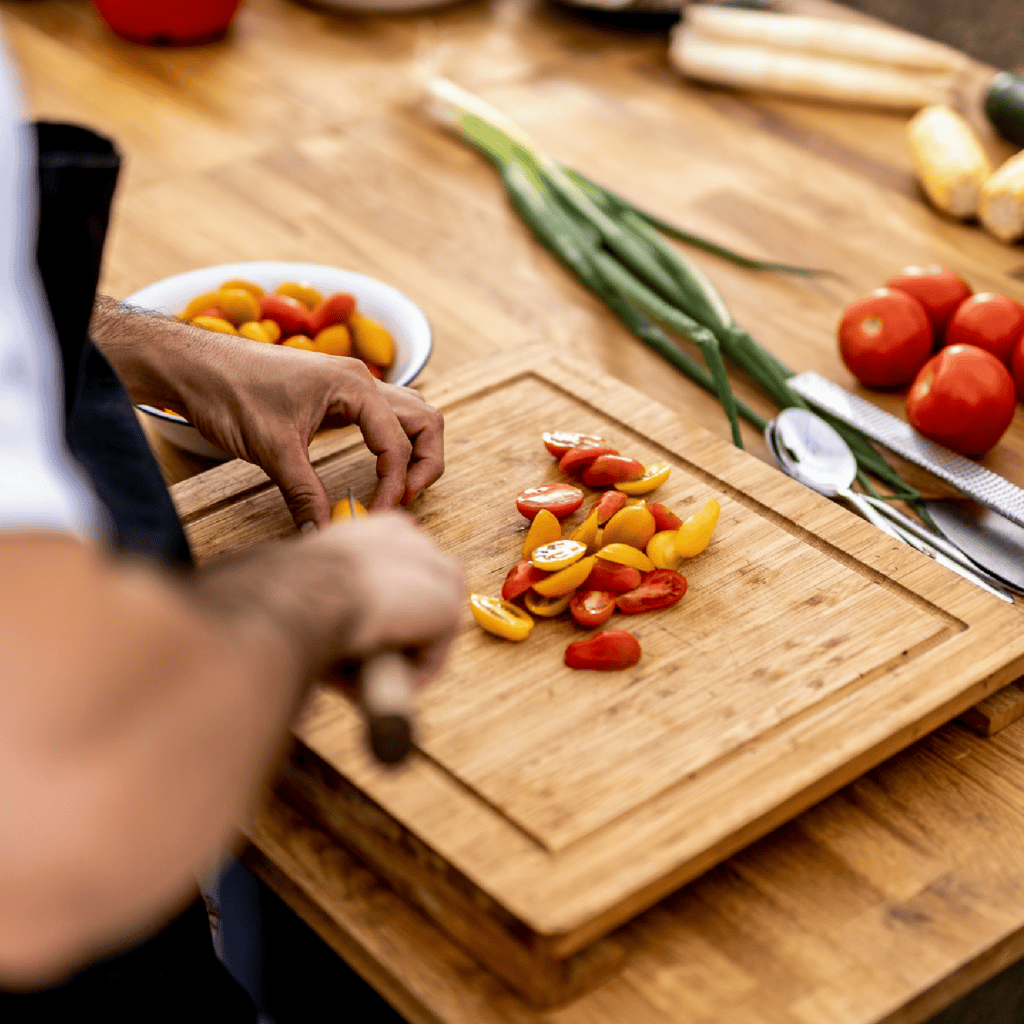 Man chopping tomatoes on a wood cutting board