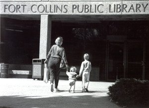 Black and white image of a woman holding hands with her two children walking into a library