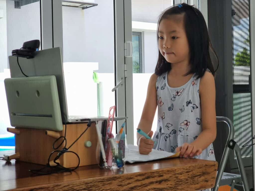 Young girl standing and looking at a laptop while writing