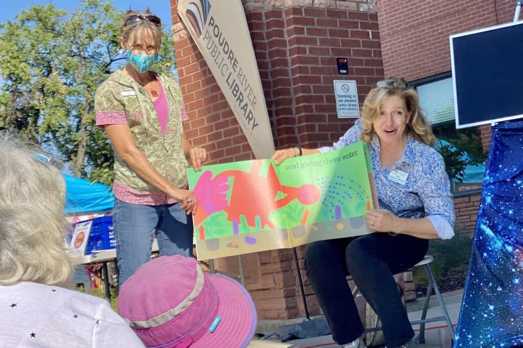 Two women presenting a book to a group of kids