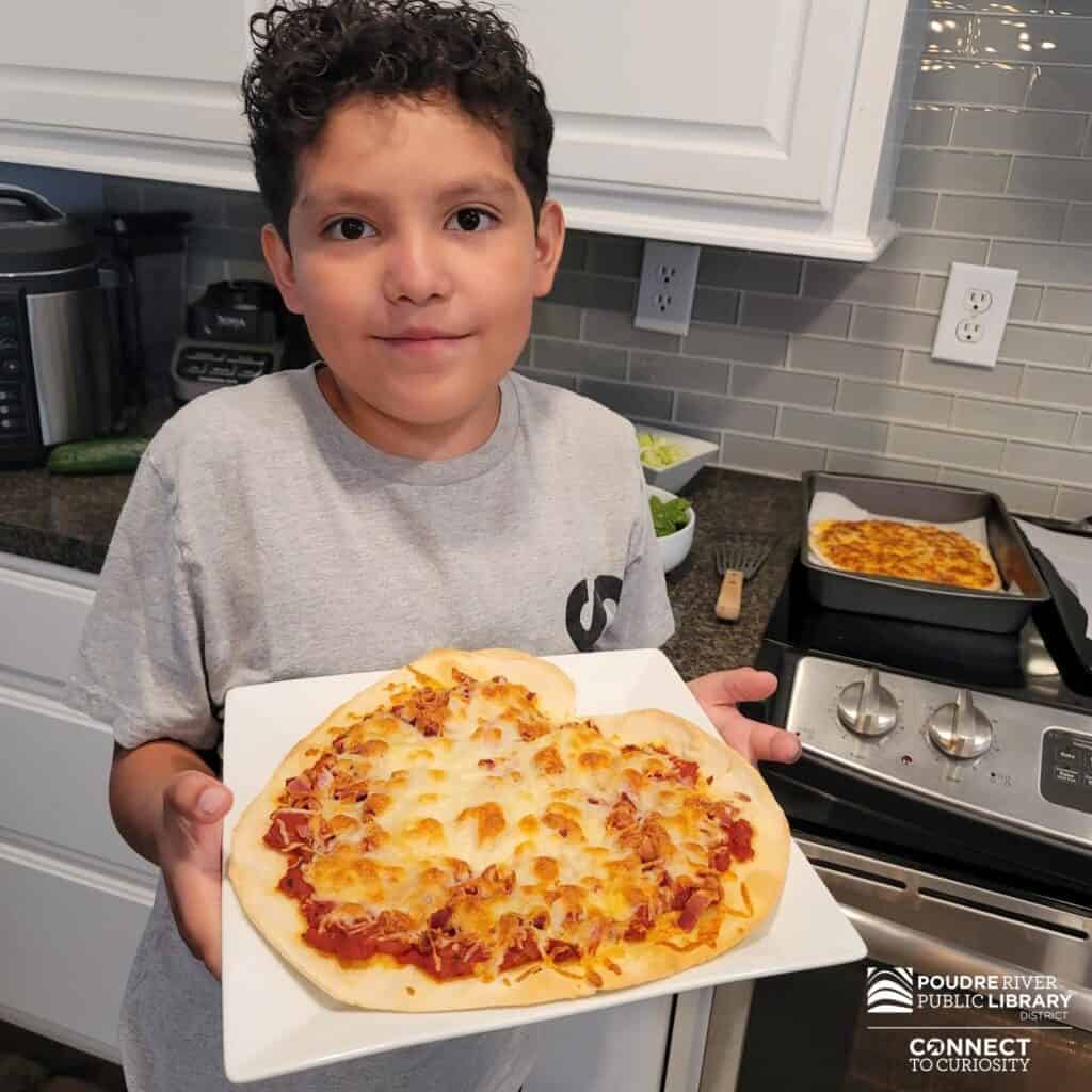 Young boy holding out a homemade pizza