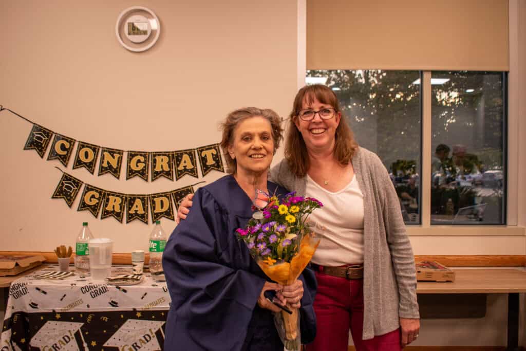 Woman in a graduation robe smiling for a picture with a friend