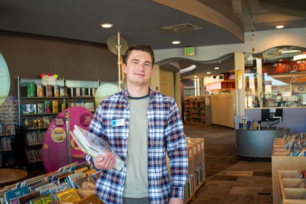 man smiling and holding a book inside a library