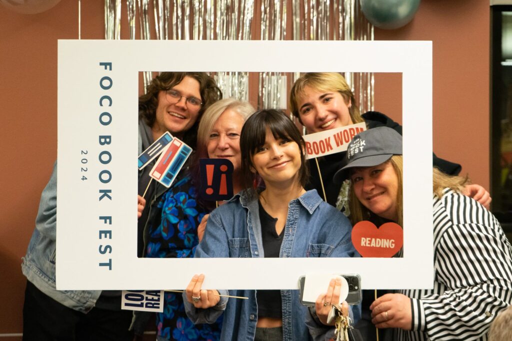 grupo de personas posando para una foto mientras sostienen un marco de la fiesta del libro de fort collins